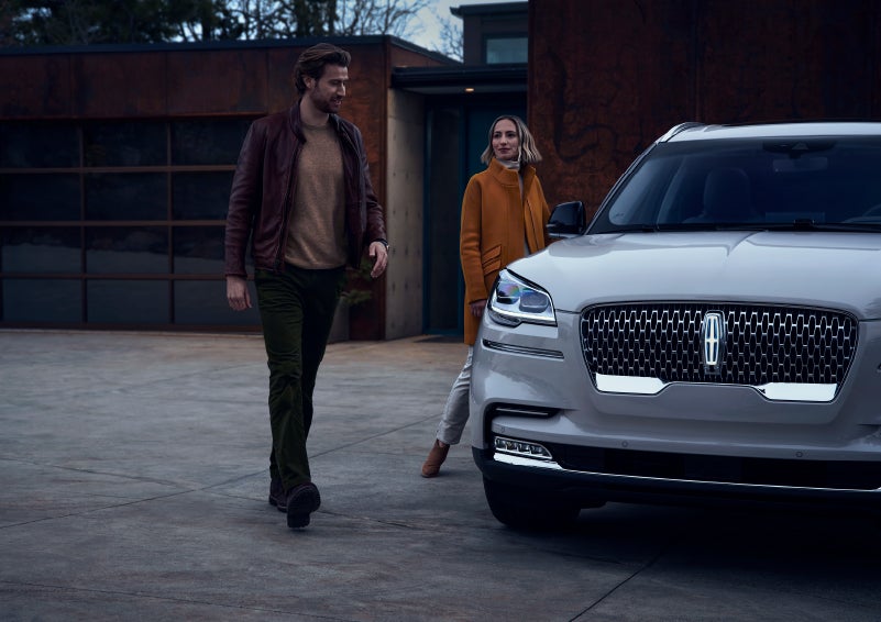 A man and a woman approaching a 2024 Lincoln Aviator® SUV, which illuminates certain lights when they are close | Biondi Lincoln in Monroeville PA
