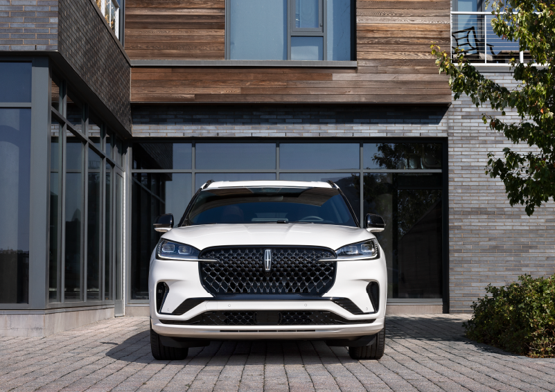 A white 2025 Lincoln Aviator® SUV is shown parked outside a modern building with gray brick and wood accents. | Biondi Lincoln in Monroeville PA