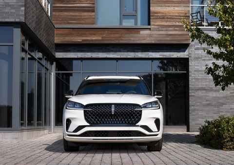 A white 2025 Lincoln Aviator® SUV is shown parked outside a modern building with gray brick and wood accents. | Biondi Lincoln in Monroeville PA