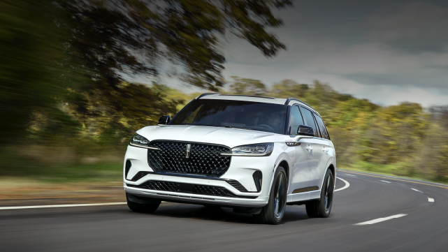 A white 2025 Lincoln Aviator® SUV is being driven down a road lined with trees. | Biondi Lincoln in Monroeville PA
