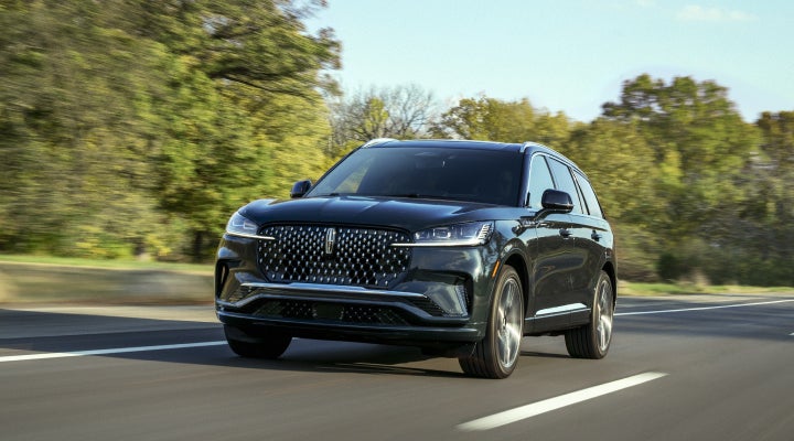 A 2026 Lincoln Black Label™ Aviator® SUV is being driven down a road lined with trees. | Biondi Lincoln in Monroeville PA