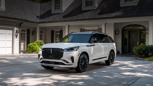 A white 2026 Lincoln Aviator® SUV is parked in the driveway of a luxury home. | Biondi Lincoln in Monroeville PA