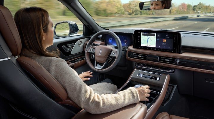 A 2027 Lincoln Aviator® SUV is being driven hands-free on a highway lined with trees. | Biondi Lincoln in Monroeville PA