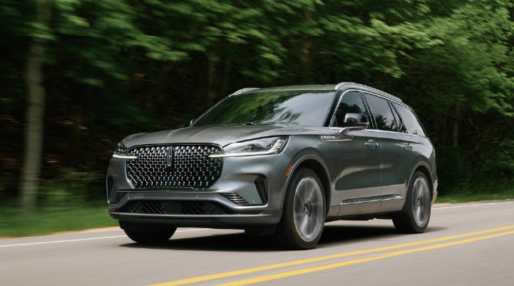 A 2027 Lincoln Aviator® SUV is being driven down a road lined with trees. | Biondi Lincoln in Monroeville PA